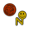 Numero Pin Pack featuring an orange vinyl record logo pin and a yellow smiley face N-shaped pin on black background